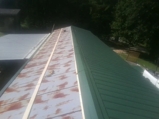 Old rusted panels beside newly installed green metal roofing — Wind Damage Roof Repair by Roofing Brothers in Medical Lake