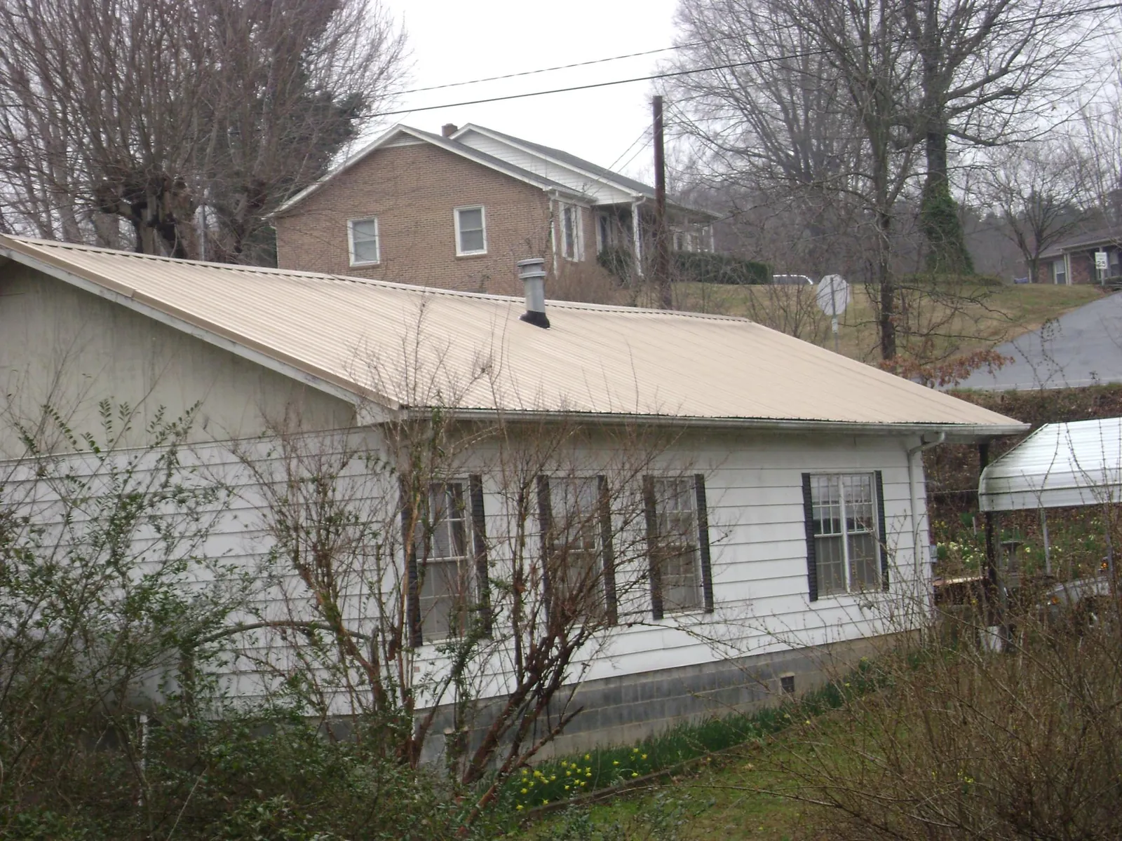 Tan metal roof on a white sided house set into a hillside — Commercial Roofing by Roofing Brothers in Medical Lake